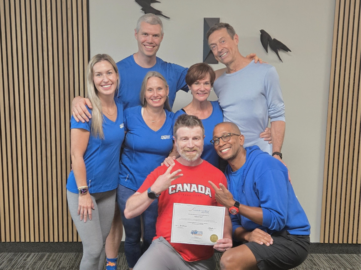 Alfred, in a red shirt and grey track pants, kneels holding his Level 3 FST certificate in Sept 2025. He is surrounded by the STW teaching team in Burlington, ON front of